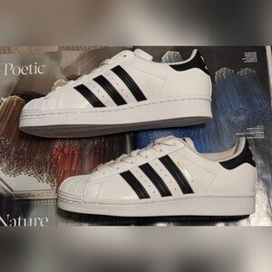 Adidas Superstar sneakers in white with black stripes and gold accents. 